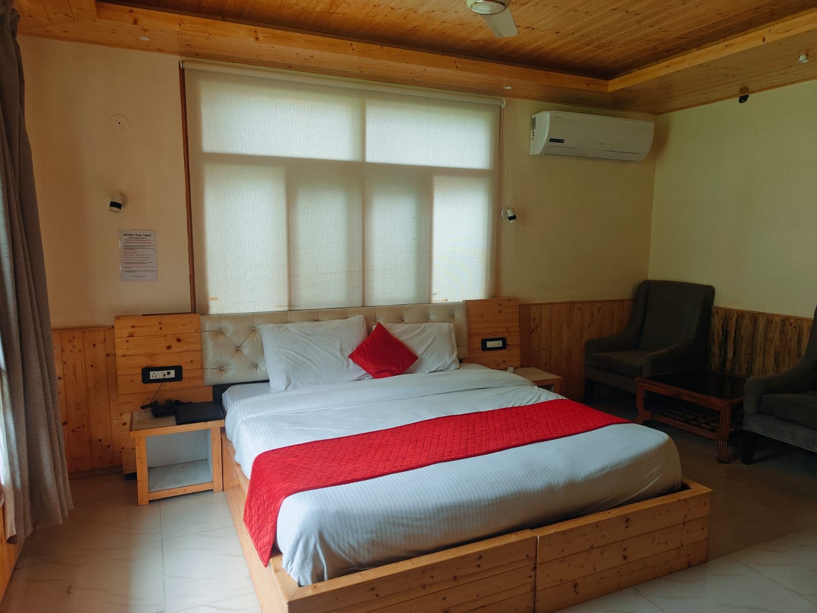 Hotellihuone, jossa on sänky, tuoli, yöpöytä ja ilmastointilaite.