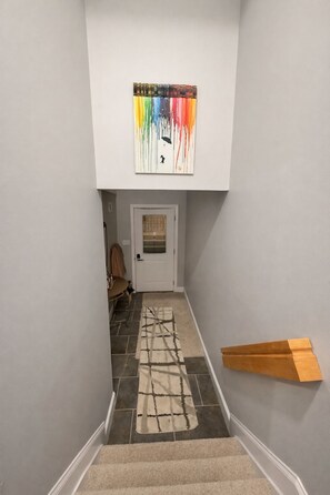 Een trap met een kamerbreed tapijt, een deur onderaan en een kunstwerk aan de muur erboven.