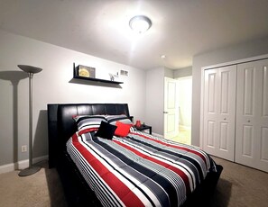 Een slaapkamer met een bed, nachtkastje, lamp, kast en een deur.