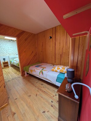 Ein Zimmer mit Holzboden, einem Etagenbett, einem kleinen Tisch mit Lampe und einer roten Wand.