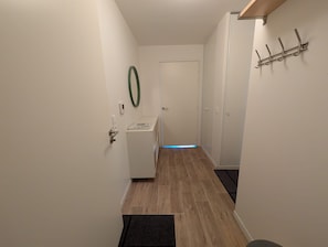 Un couloir avec une porte au fond, un porte-manteau et un luminaire fixé au mur.