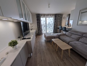 Un salon moderne comprenant un téléviseur à écran plat, un canapé, une table basse et un coin repas avec des chaises.
