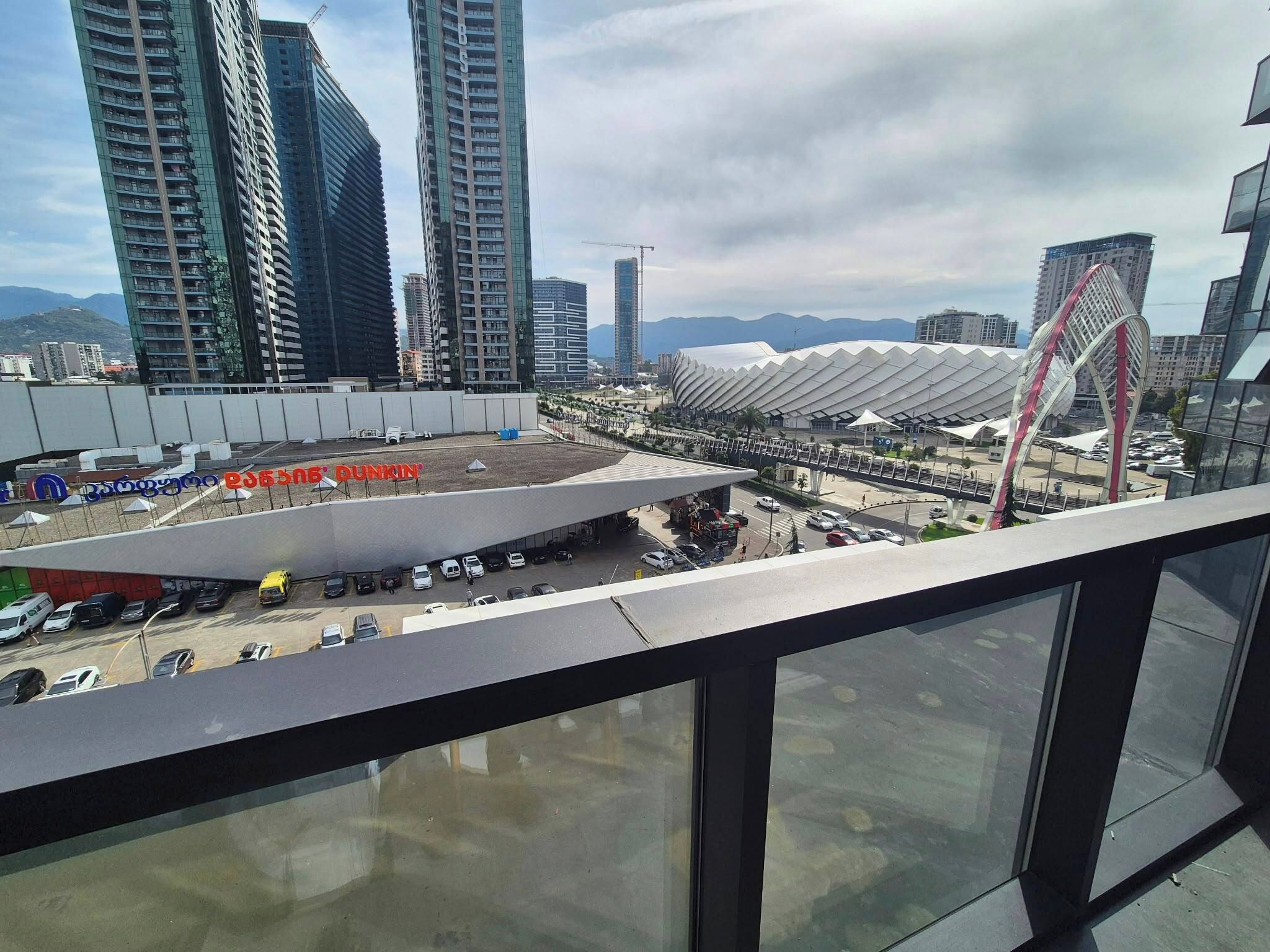 Vista de una zona urbana moderna con edificios altos, un estadio y un estacionamiento.