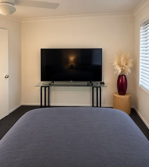 A bedroom with a bed, a TV on a glass stand, a vase with dried plants, and a window with blinds. - Cosy suburban townhouse (Acacia Ridge)