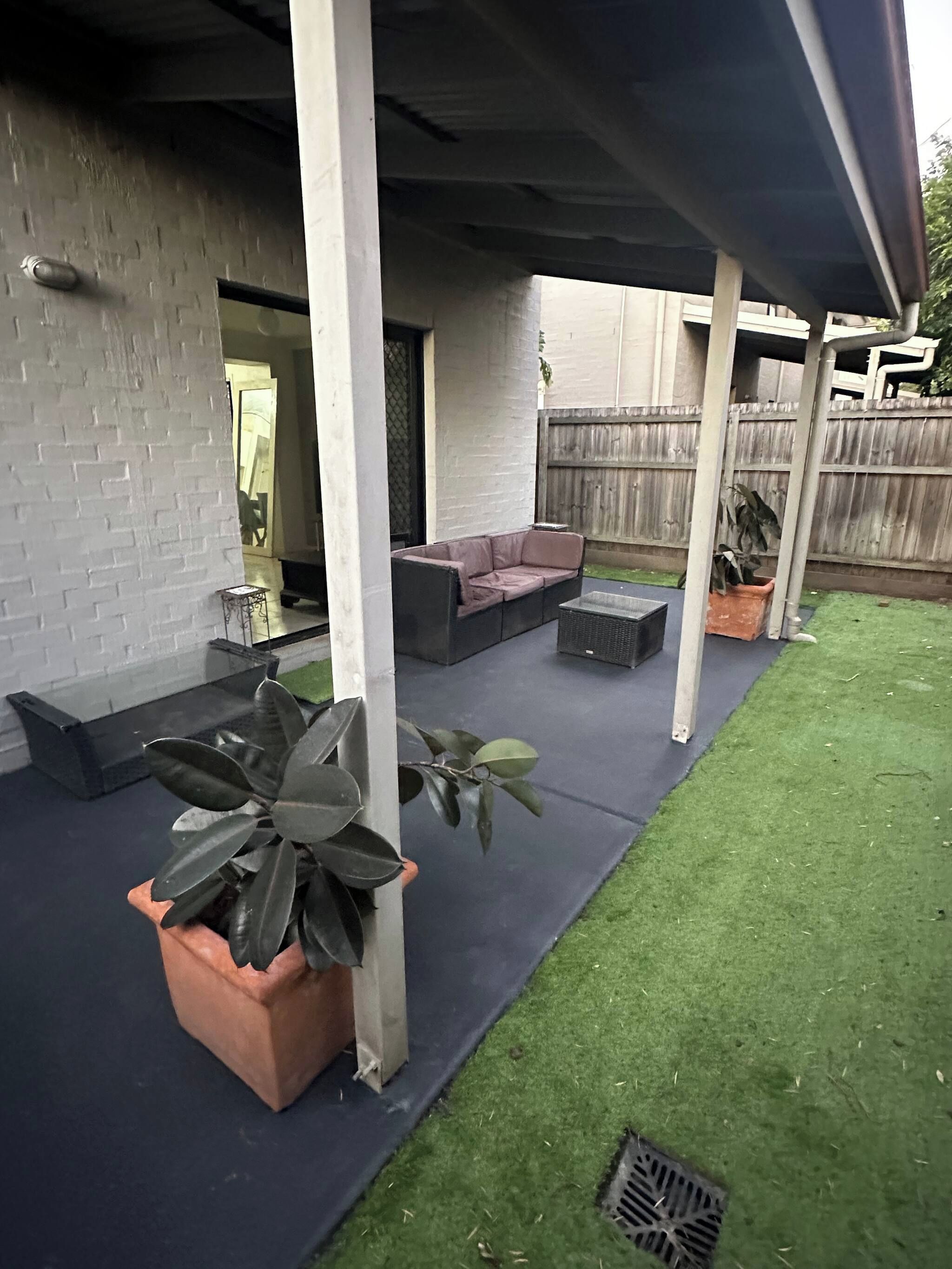 A covered outdoor patio with a sectional sofa, a small table, and potted plants.