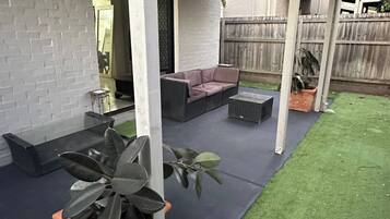 A covered outdoor patio with a sectional sofa, a small table, and potted plants.
