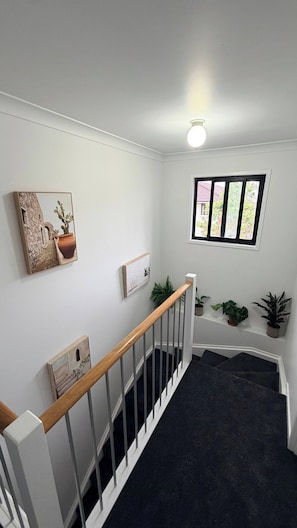 A staircase with a wooden handrail leading to a landing with a window and potted plants. - Cosy suburban townhouse (Acacia Ridge)