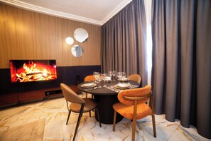 A dining area with a round table set for four, a flat-screen TV displaying a fire, and a modern interior design with a marble floor. - New Listing (Lomé)