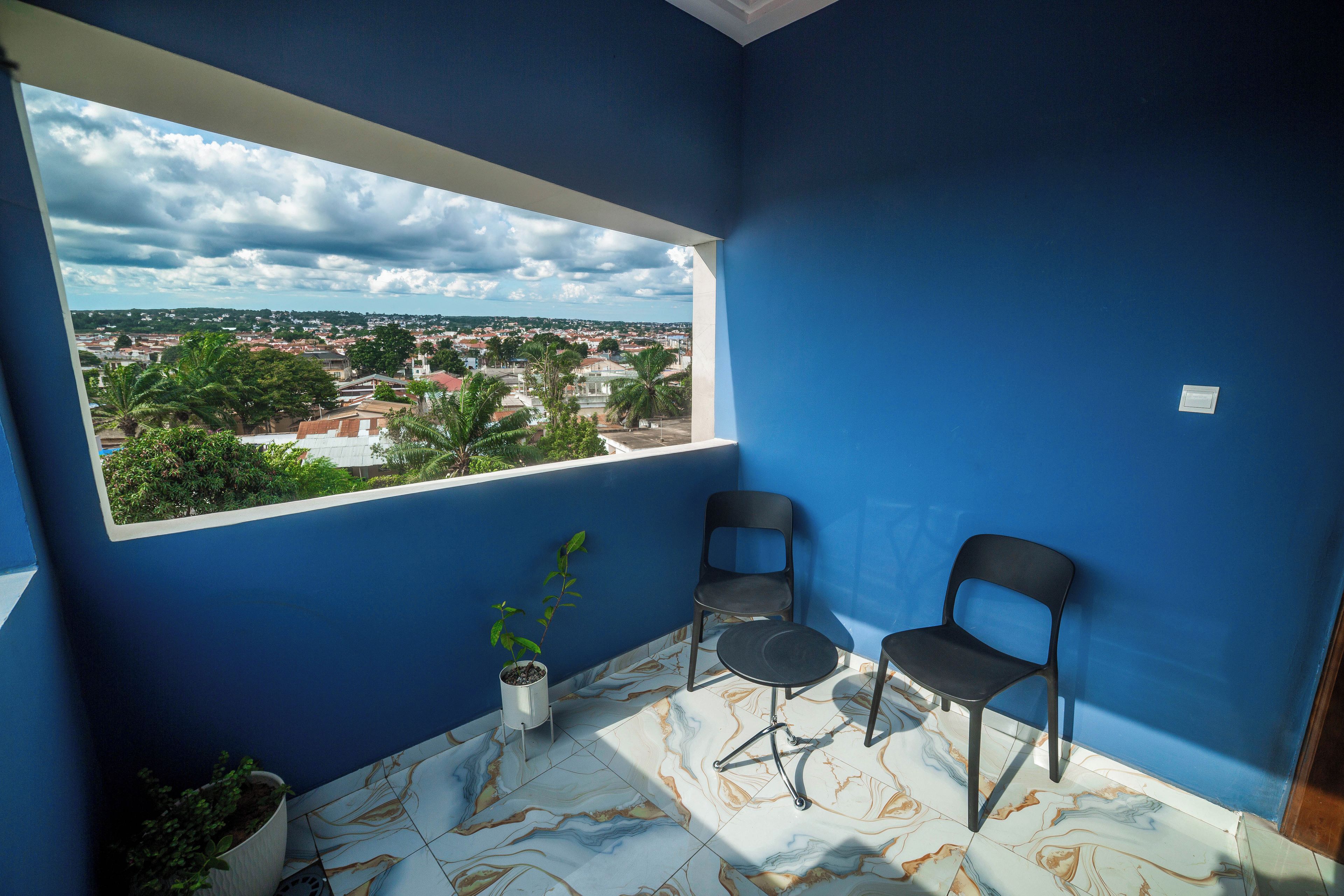 A room with a large window, two chairs, a potted plant, and a view of a cityscape.