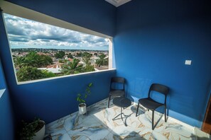 A room with a large window, two chairs, a potted plant, and a view of a cityscape. - New Listing (Lomé)