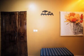 A room with a wooden door, a wall-mounted light switch, a small shelf with a silhouette decoration, and a framed painting of flowers. - New Listing (Lomé)