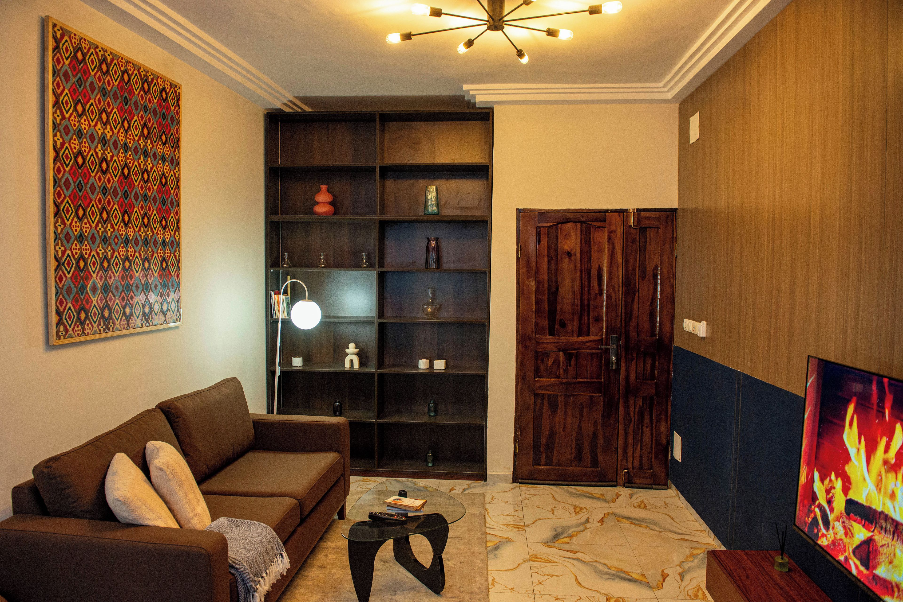 A living room with a brown sofa, a glass coffee table, a bookshelf, and a wooden door.