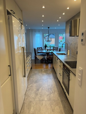 Cozinha moderna com ilha central, eletrodomésticos de aço inoxidável e área de jantar com cadeiras e mesa.
