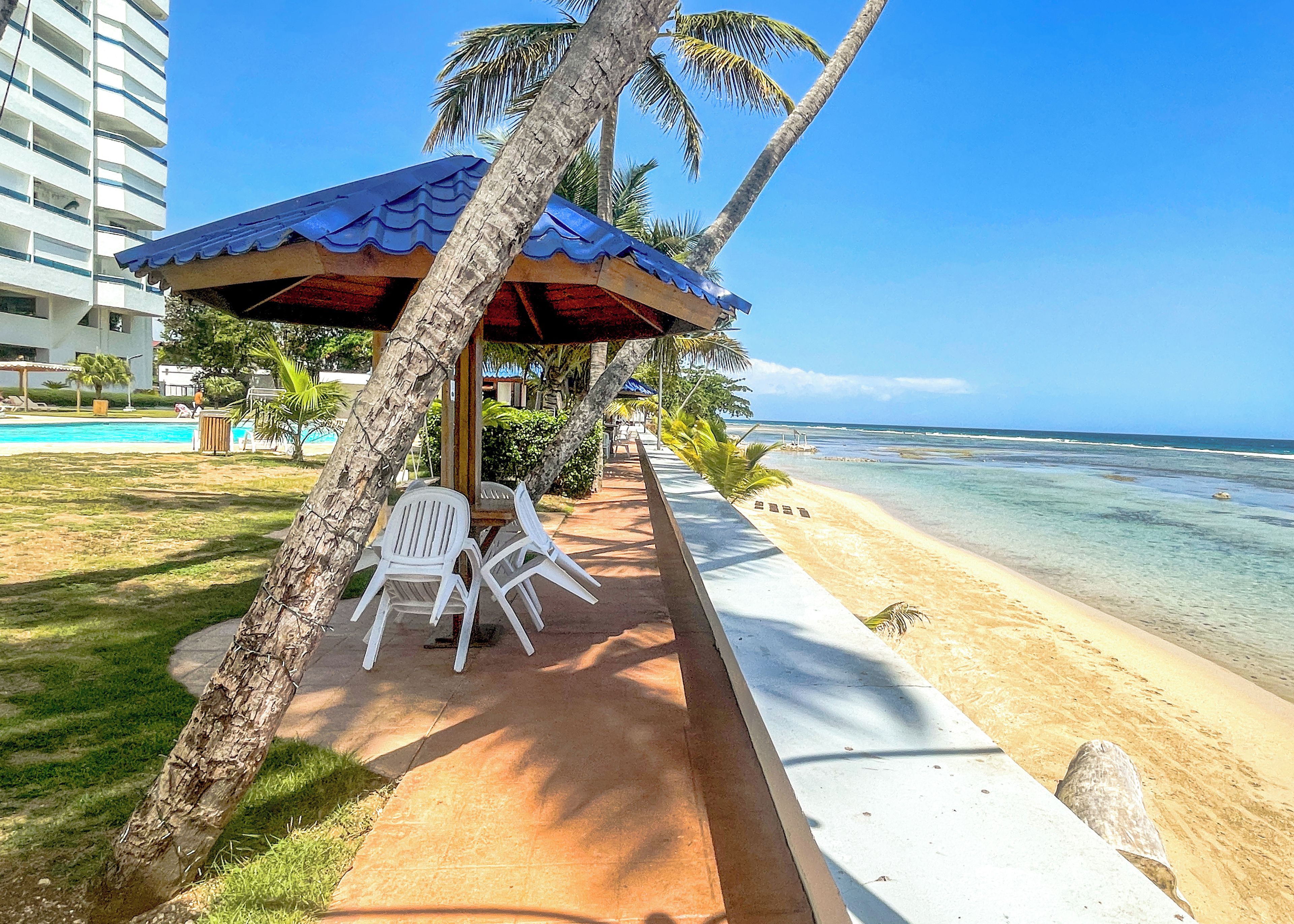 Un complexe hôtelier situé en bord de mer, doté d’une piscine, de chaises longues et offrant une vue sur l’océan.