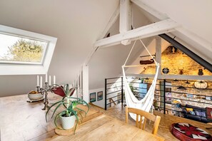Un dormitori tipus loft amb terra de fusta, una cadira de corda, una taula de menjador amb espelmes i una vista de la cuina inferior.