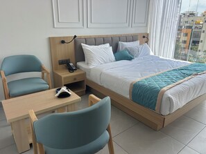 A hotel room with a bed, two chairs, a small table, and a nightstand with a phone. - Hotel Velvet Blue Reva Circle Airport rd (Bengaluru)