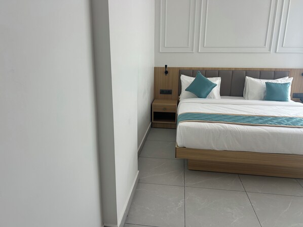 A hotel room with a bed, nightstand, and a wall with paneling. - Hotel Velvet Blue Reva Circle Airport rd (Bengaluru)