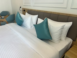 Uma cama bem arrumada com roupa de cama branca e almofadas verde-água, uma cabeceira de madeira e uma pequena mesa de cabeceira de madeira.
