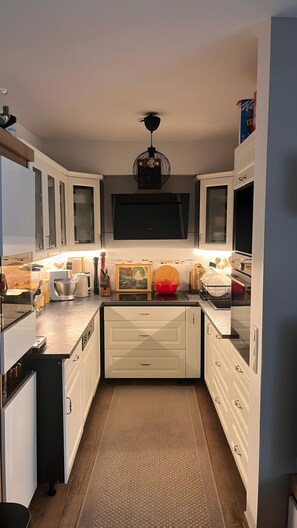Una cocina compacta con armarios blancos, una isla central y una lámpara colgante moderna.
