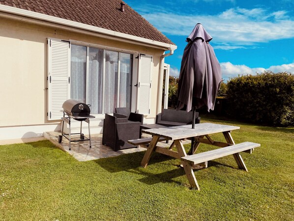 Eine Terrasse mit Grill, Gartenmöbeln und Sonnenschirm.