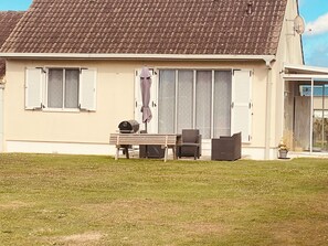 Ein Haus mit einem Ziegeldach, einer Terrasse mit Tisch und Stühlen sowie einer Schiebeglastür.