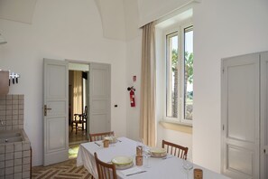 A dining area with a table set for two, a kitchen area with a sink, and a view of the outdoors through a window. - Luxury 5-bedroom country house with AC in charming Puglia inthe heart of Salento (Puglia)