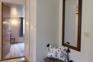 Ein Flur mit einer Holztür, die zu einem Raum führt, der mit Blumenpapier tapeziert ist, mit einem Spiegel und einer Bank mit einem Blumenkissen.