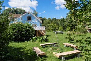 Ein blaues Haus mit einer Terrasse, umgeben von üppigem Grün und blauem Himmel.