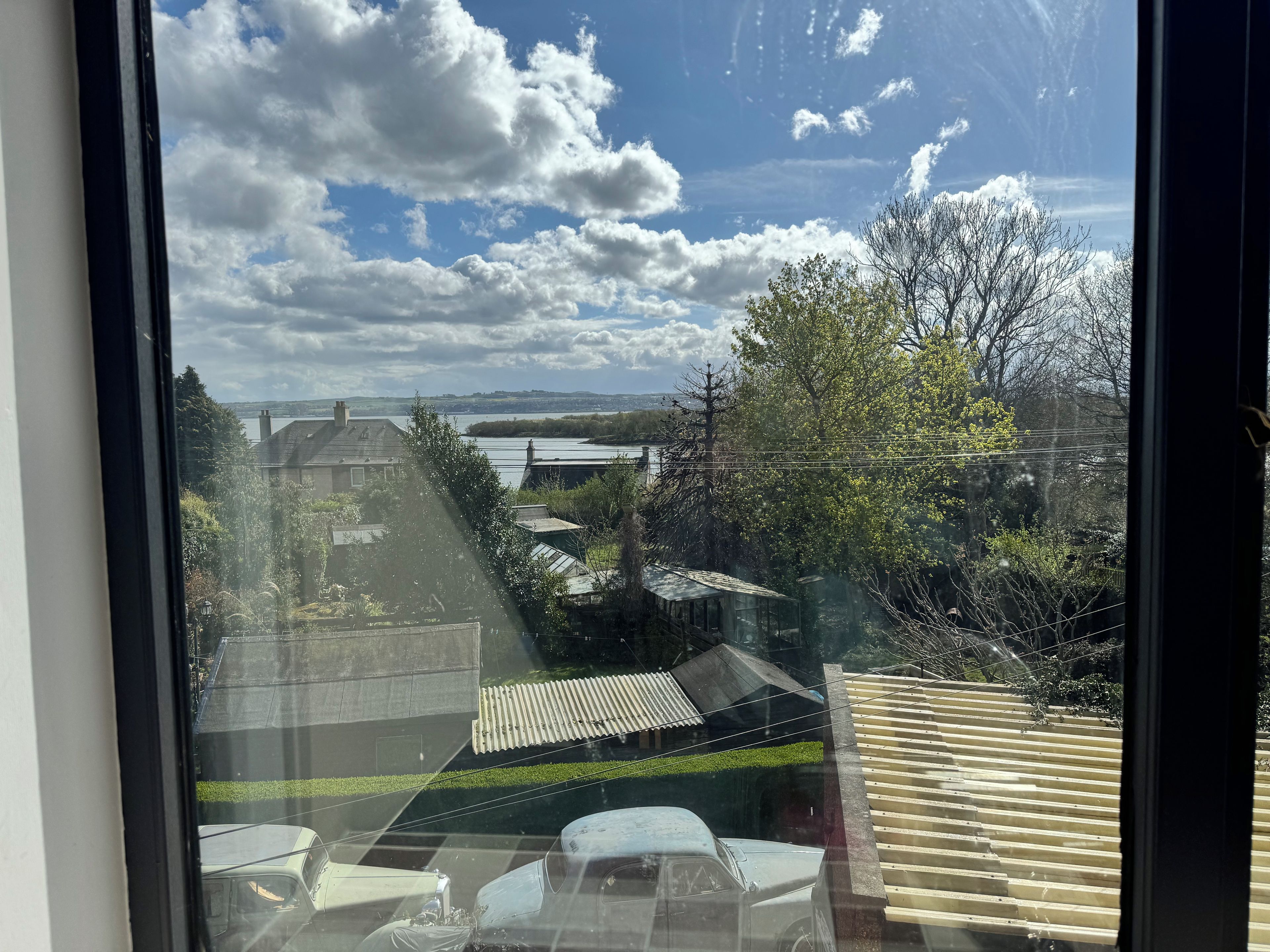 A view through a window with a clear sky, a body of water, and buildings in the distance.