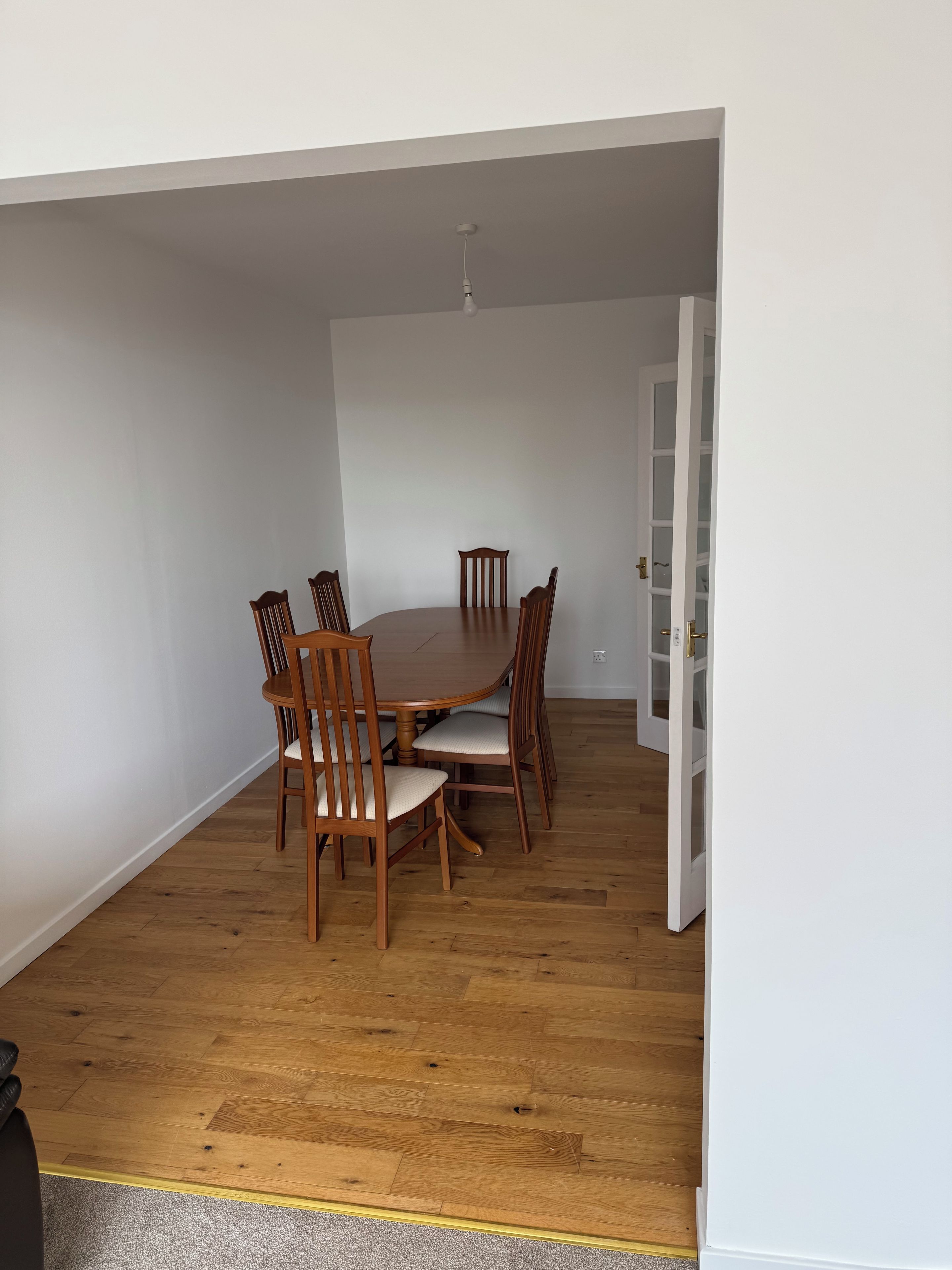 A dining area with a round table and six wooden chairs, a white door, and a wooden floor.