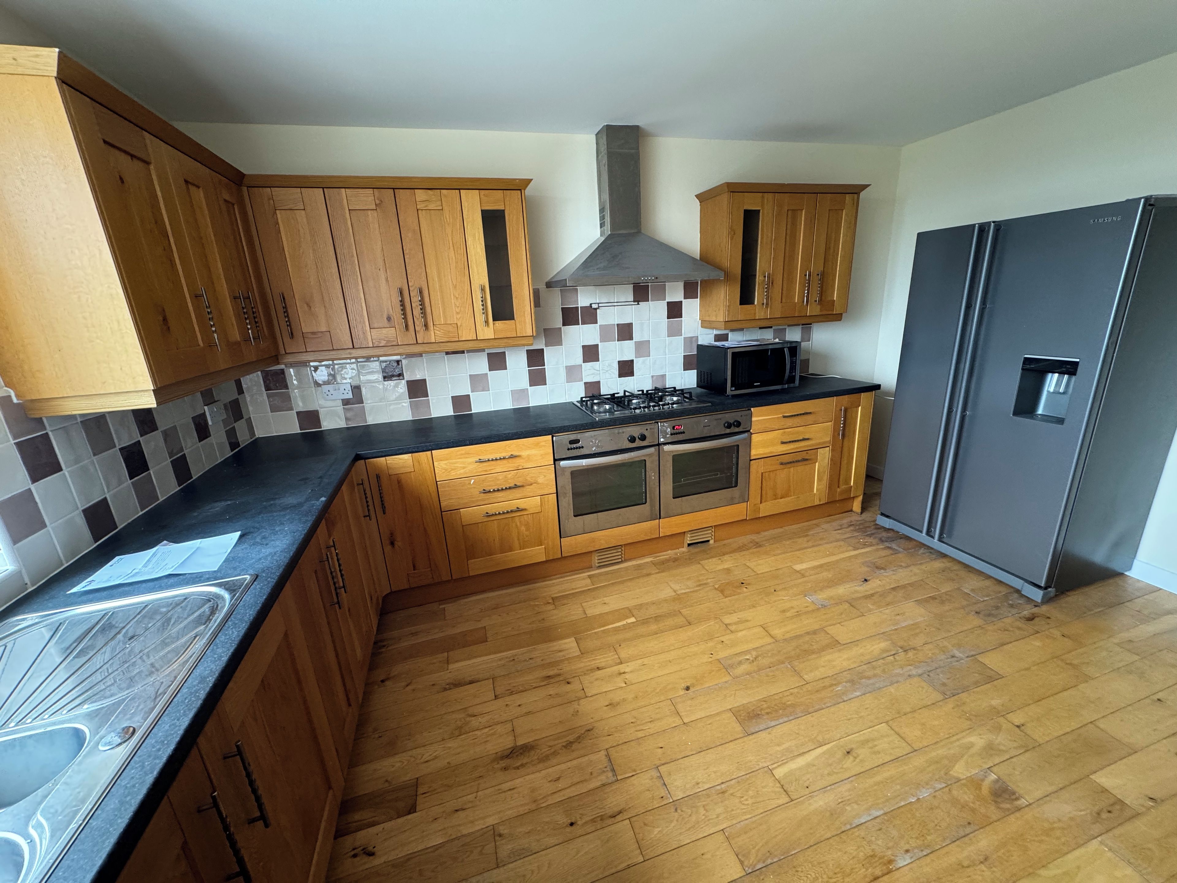 A kitchen with wooden cabinets, a gas stove, an oven, a microwave, and a refrigerator.