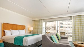 Una habitación de hotel con cama, sofá, lámpara y vistas a edificios desde la ventana.