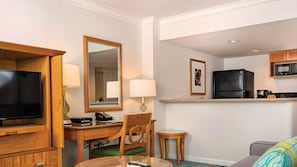 Habitación de hotel con televisión, escritorio, silla, kitchenette y sofá.