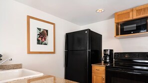 Eine Küche mit einem schwarzen Kühlschrank, einer Mikrowelle, einer Kaffeemaschine und einem gerahmten Bild an der Wand.