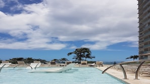 Una piscina con sillas de descanso y una palmera, rodeada por un edificio de gran altura.