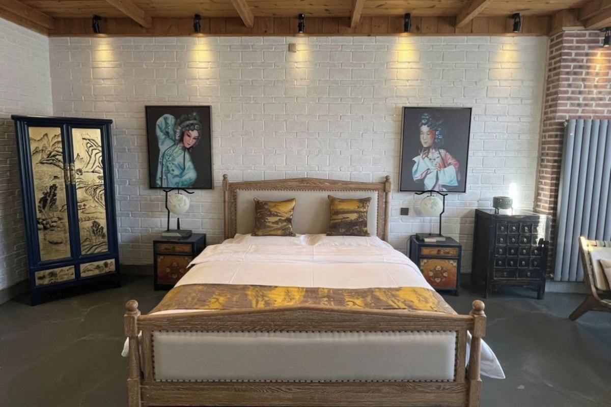 A bedroom with a wooden bed, white brick walls, and artwork on the walls.