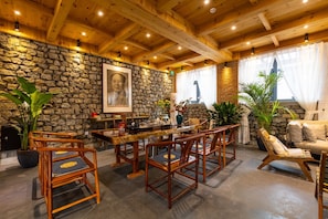 A rustic interior with a stone wall, wooden ceiling beams, a dining area with chairs and a table, and a sofa. - Mutianyu Great Wall Castle Homestay (Huairou)