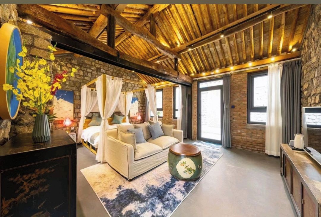 Ein gemütliches Zimmer mit Steinwand, Holzboden, einer Couch, einem runden Tisch und einem großen Fenster.