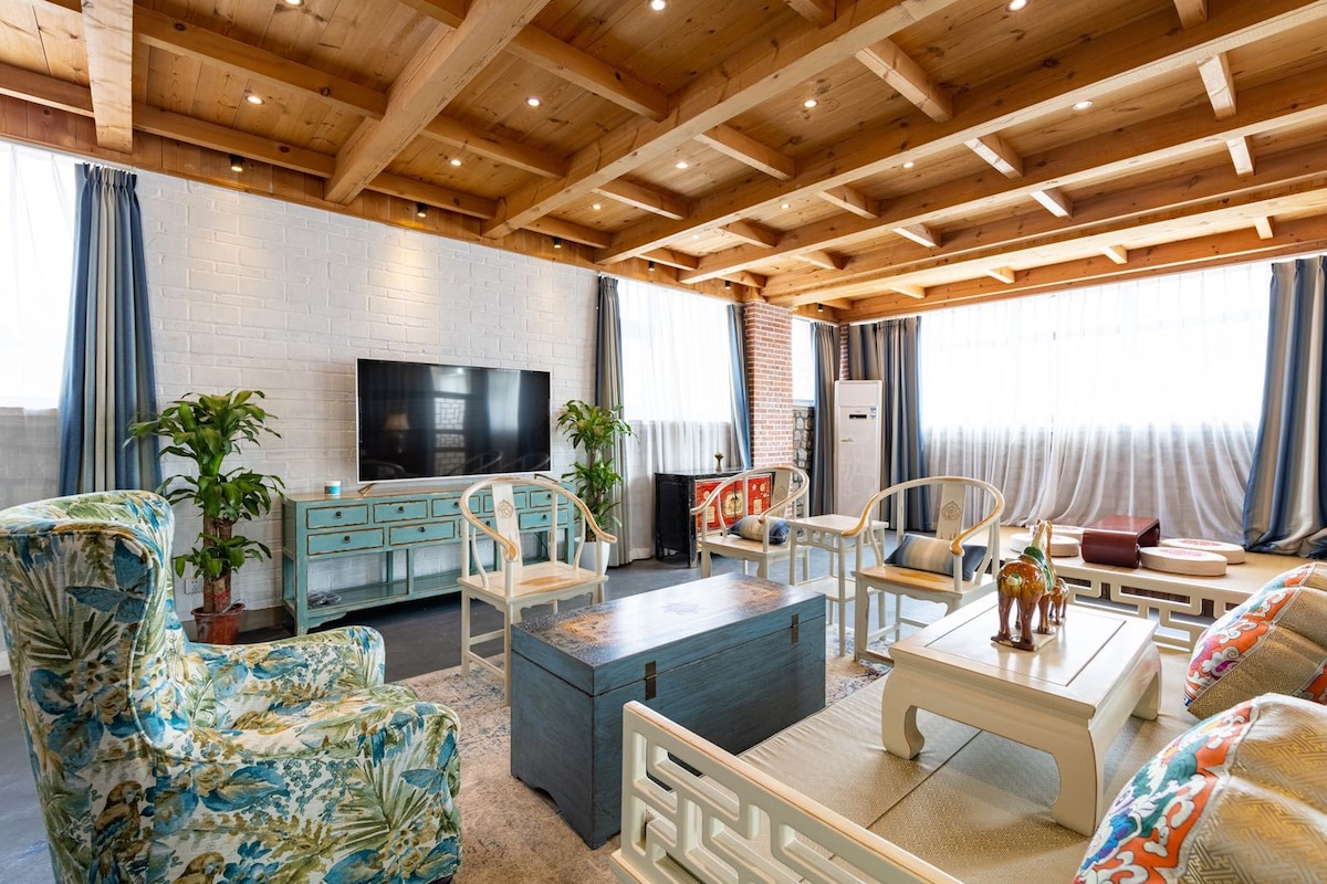A spacious living room with a high wooden ceiling, a television, and seating arrangements.