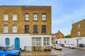 A two-story brick building with a white facade, a blue door, and a small front garden.