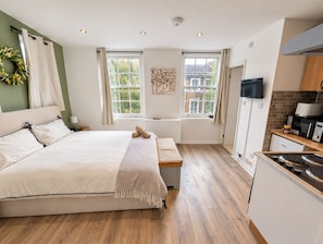 A modern bedroom with a large bed, bedside tables, a bench, and a view of the city through windows.