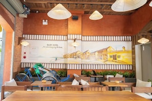 A restaurant with wooden tables and chairs, a mural of a street scene, and a bicycle parked outside. - Sujet Hotel Da Nang (Da Nang Municipality)