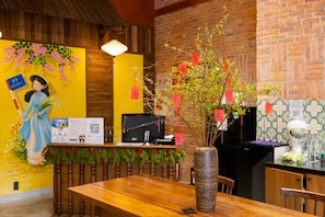 A reception area with a wooden desk, a vase with branches, and a mural on the wall. - Sujet Hotel Da Nang (Da Nang Municipality)