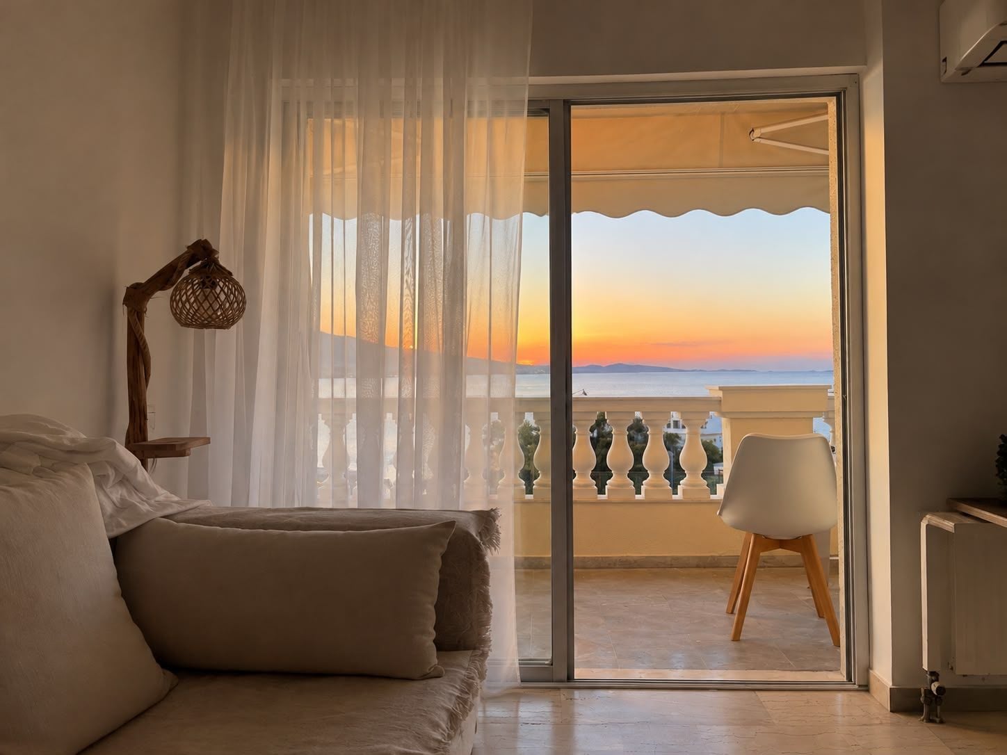 A bedroom with a balcony, a bed with pillows, a chair, and a lamp.