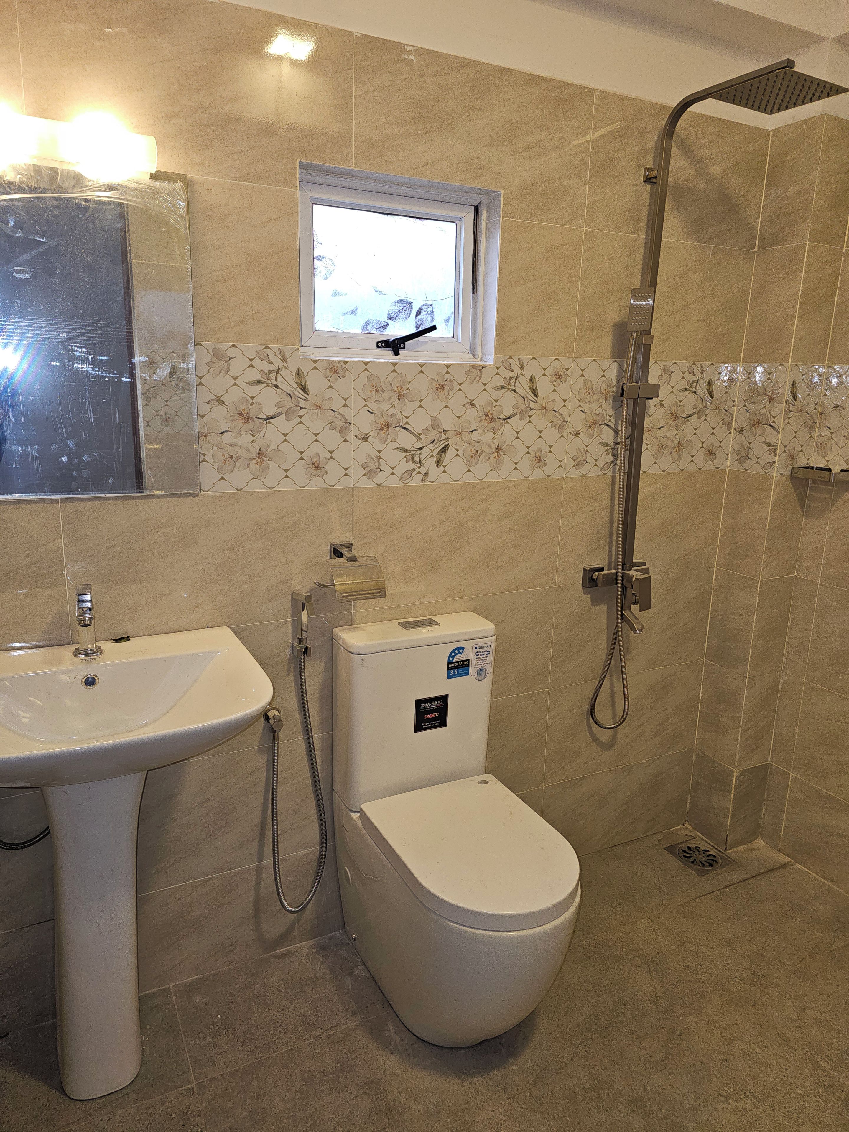 A bathroom with a pedestal sink, a toilet, a shower, and a window.