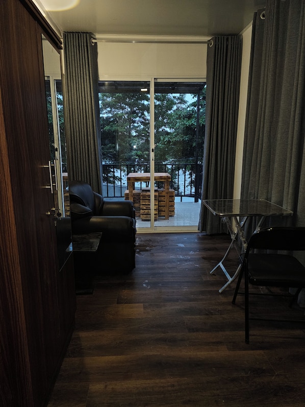 A room with a sliding glass door leading to an outdoor area, a black leather sofa, a small wooden table, and a metal-framed chair.