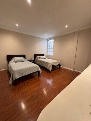 Une chambre avec deux lits, un plancher en bois et une fenêtre.