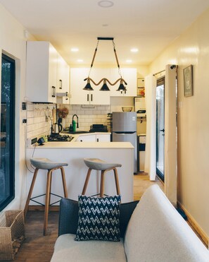 A compact kitchen with a central island, bar stools, and a hanging light fixture.