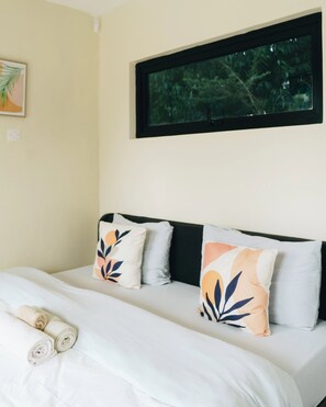 A bed with a headboard, two pillows, and rolled towels.