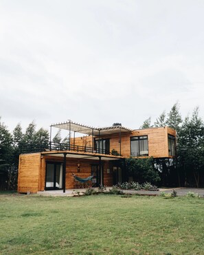 A modern wooden house with a covered patio and a hammock.